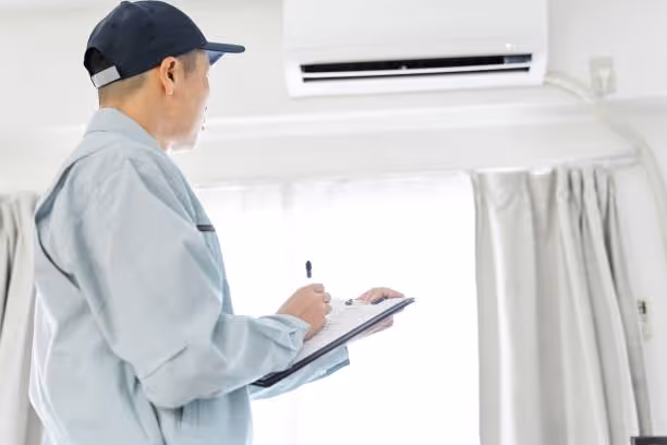 Technician checking air conditioning unit with clipboard near curtained window
