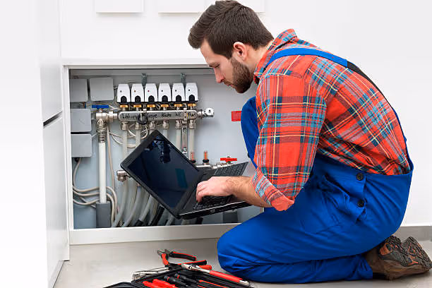 Technician checking heating system manifold with laptop and tools