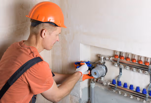 Worker in orange helmet inspects plumbing manifold for heating system installation