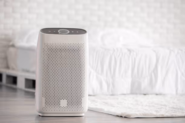 White air purifier on floor near bed in minimalist bedroom setting