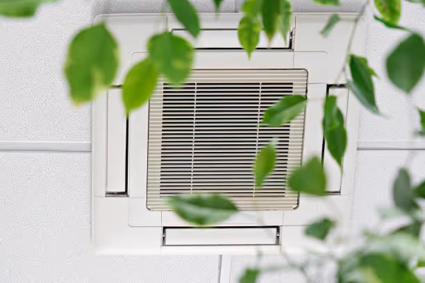 Air vent with green leaves blurred in foreground on white wall