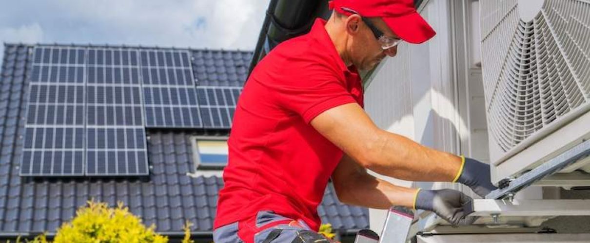 Technician in red checking solar panels and air conditioning unit on roof