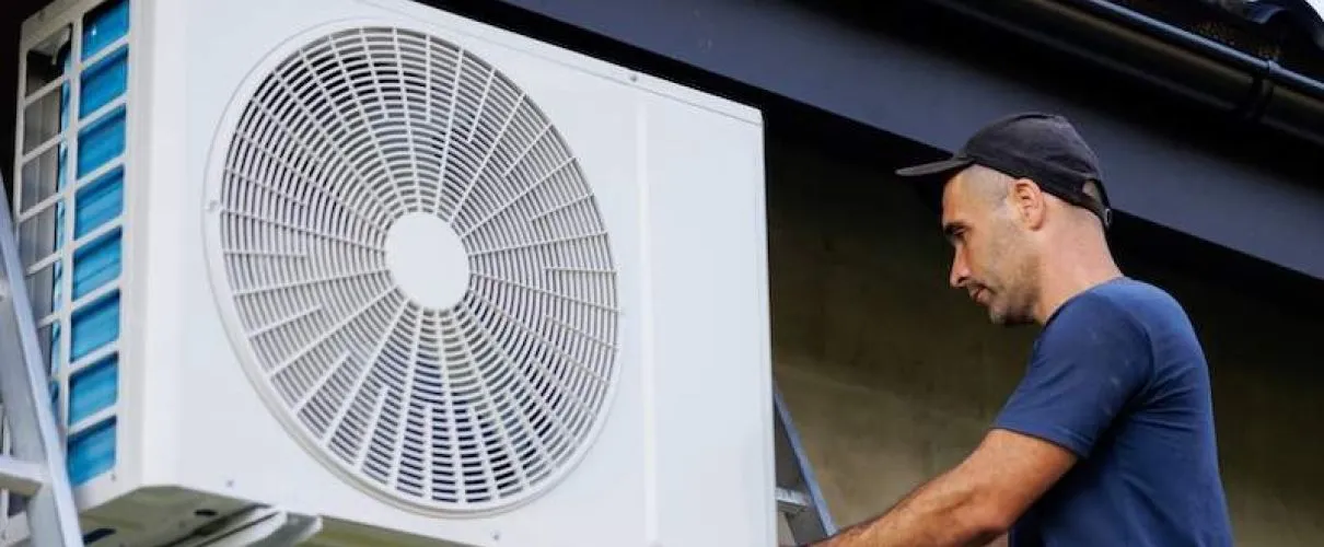 Technician installing or repairing a large white air conditioning unit outside
