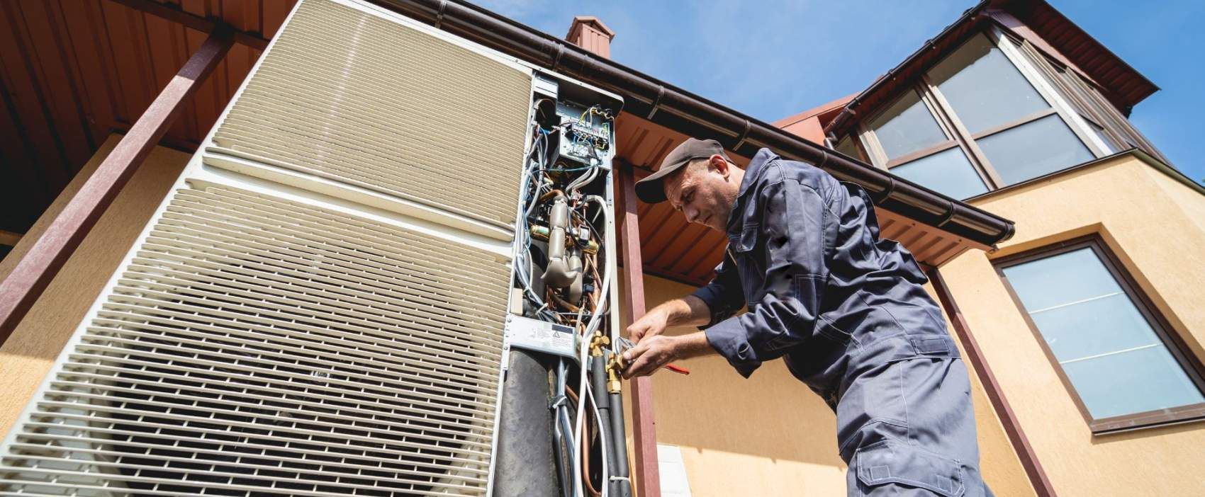 Technician repairing an outdoor air conditioning unit on a residential building