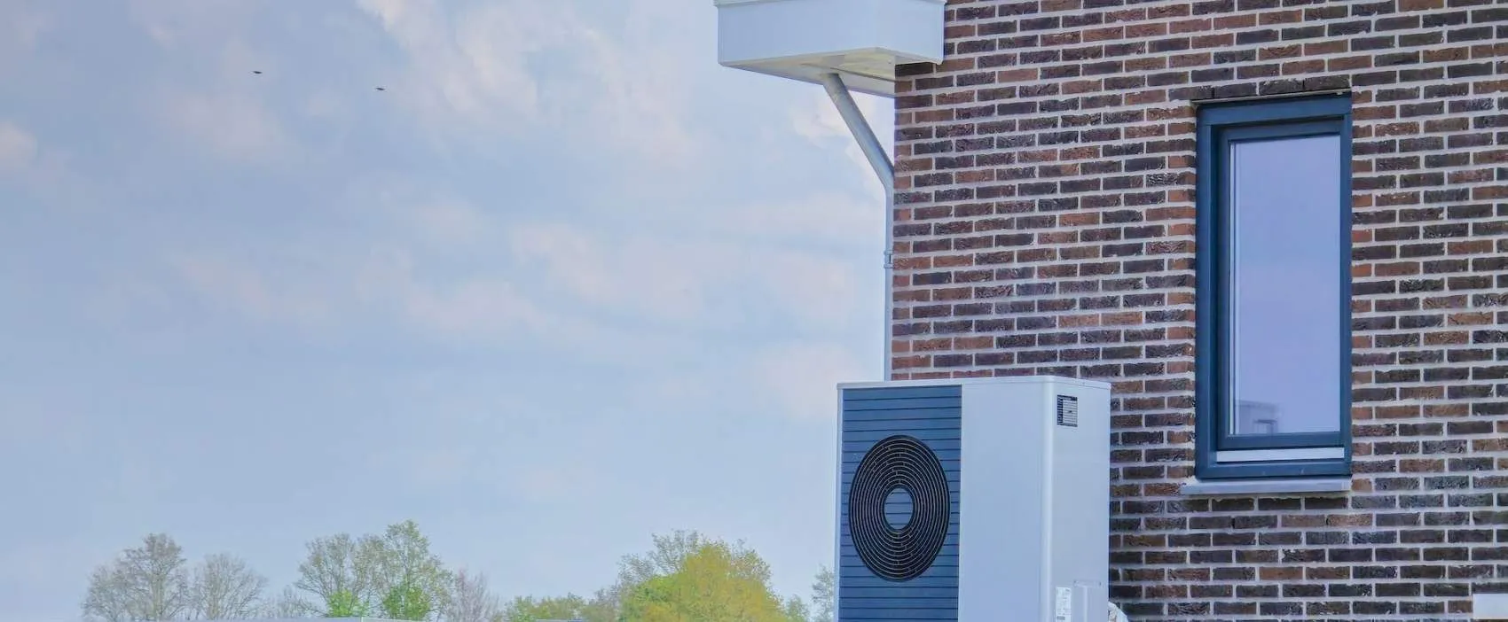 Blue heat pump installed on brick wall with trees and sky background