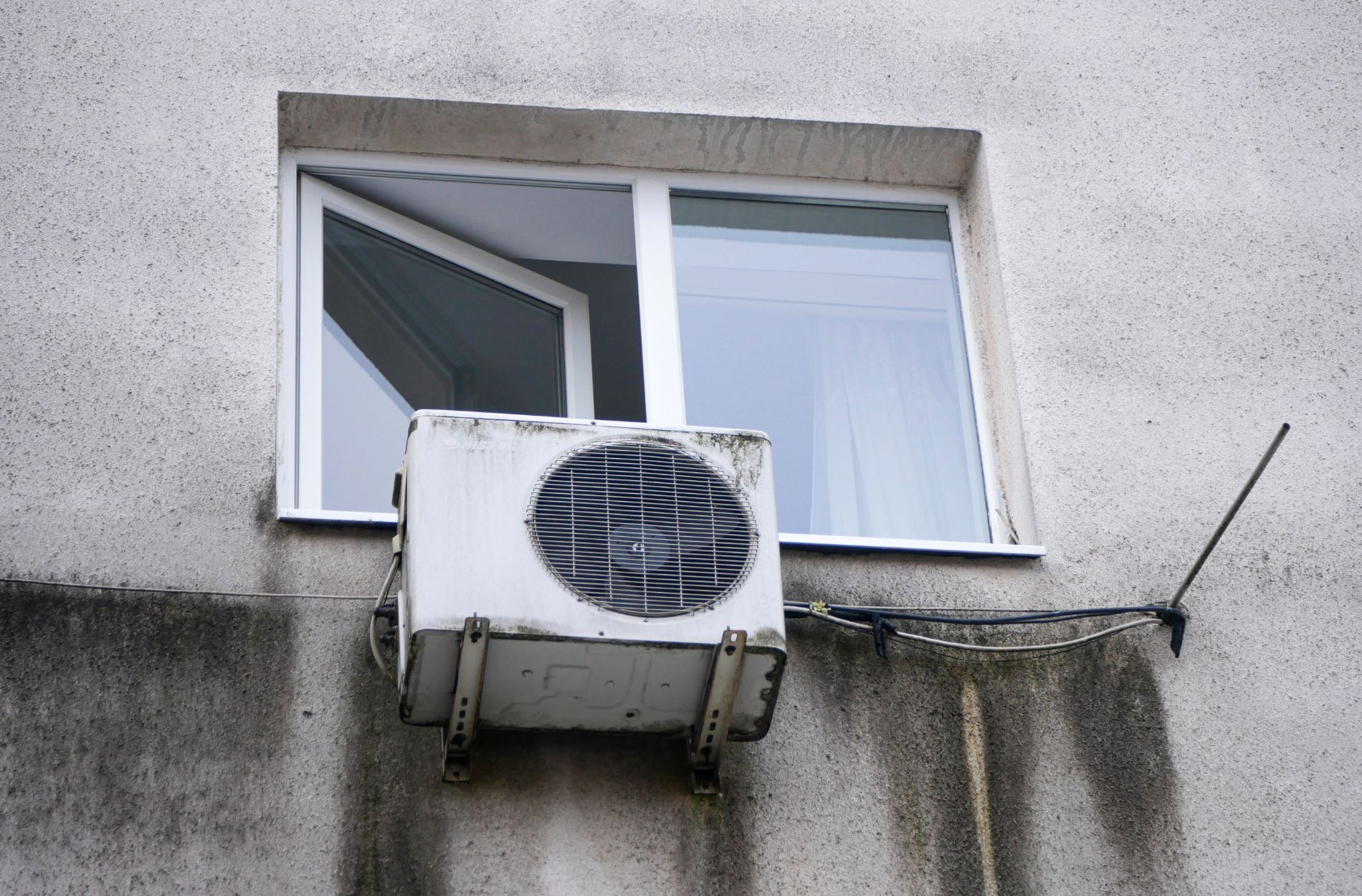 White air conditioning unit mounted beside a window on a textured wall