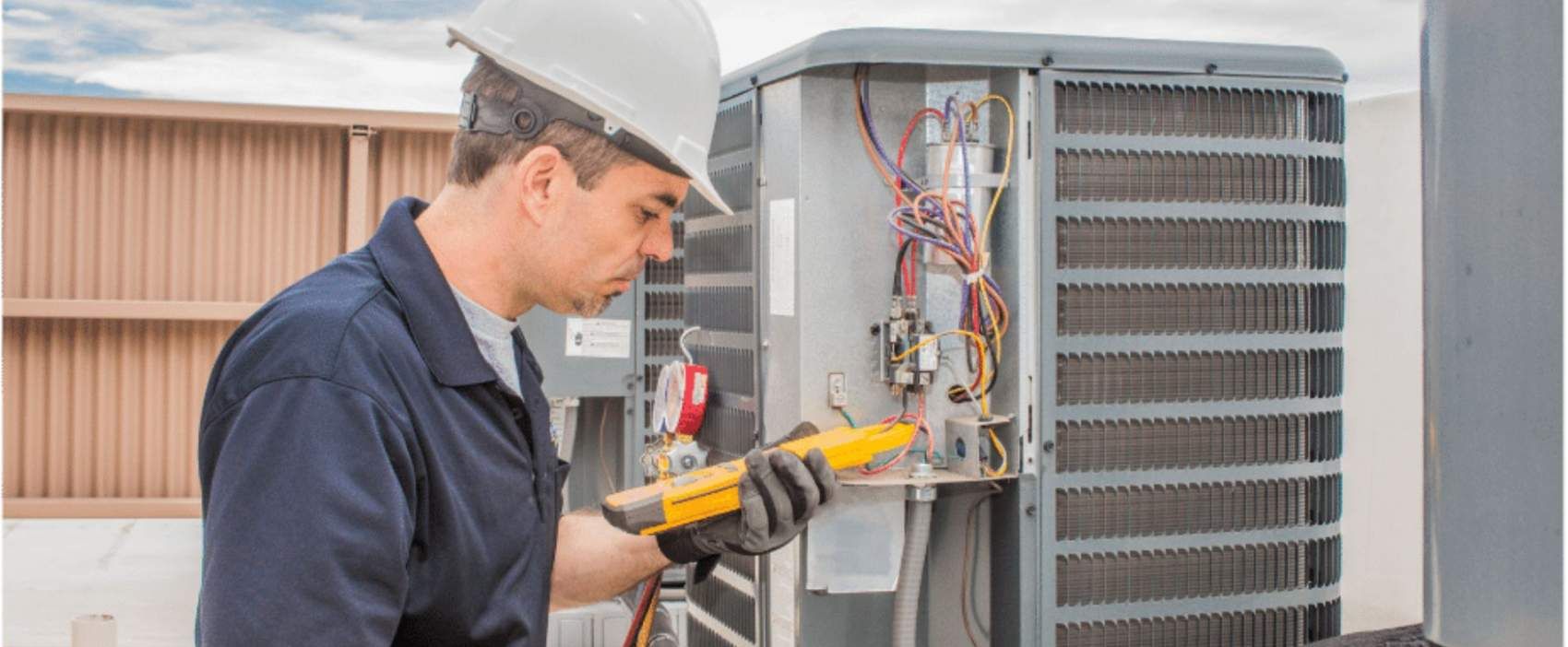Technician in hard hat checking electrical connections on HVAC unit