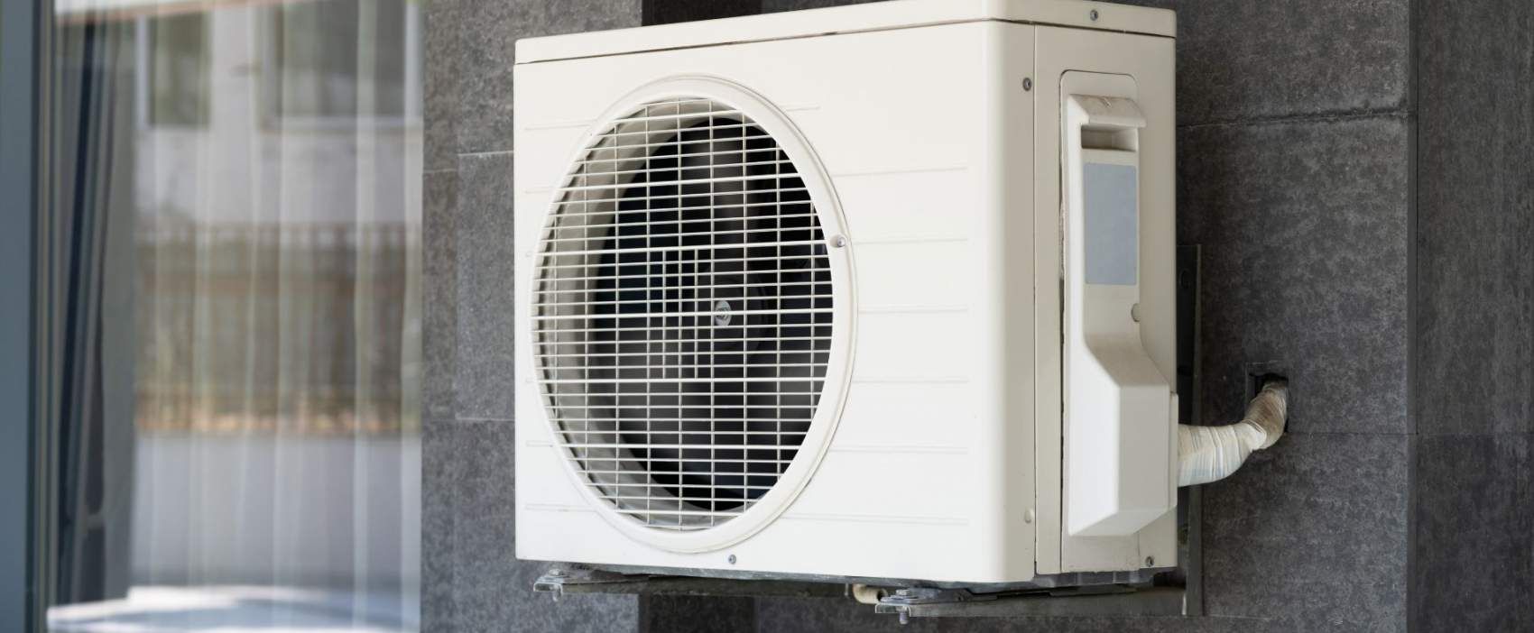 White air conditioning unit mounted on gray exterior wall with grille