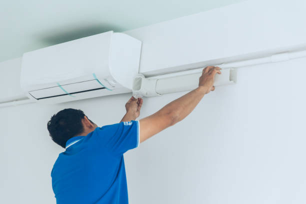 Technician in blue shirt installing or repairing a white air conditioning unit