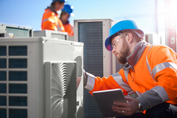 Workers in safety vests inspect industrial equipment with digital tablet