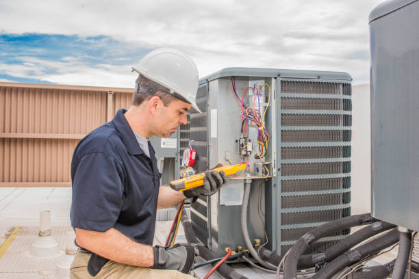 Technician in hard hat checking electrical connections on HVAC unit