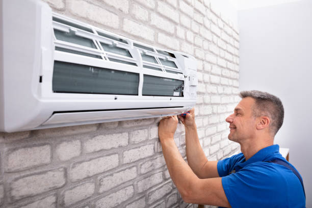 Technician installing or repairing white air conditioning unit on brick wall