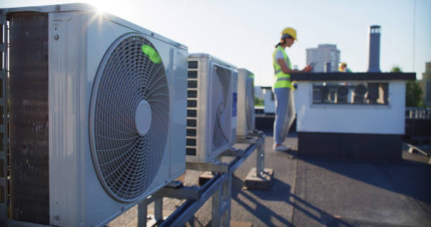 Worker in safety vest inspects air conditioning units on rooftop