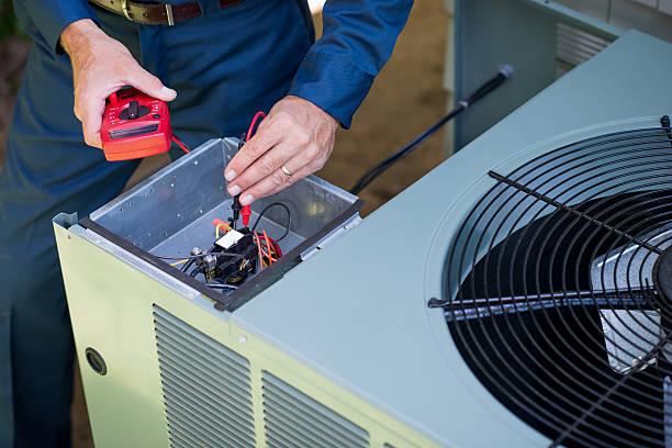 Technician repairing HVAC unit, using multimeter to check electrical connections