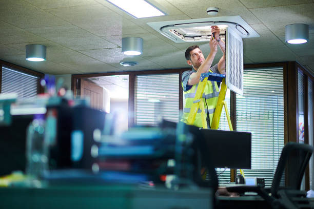 Worker in safety vest checking ceiling light fixture in office
