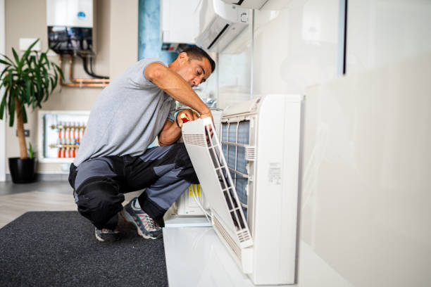 Technician crouching and repairing air conditioning unit in indoor setting