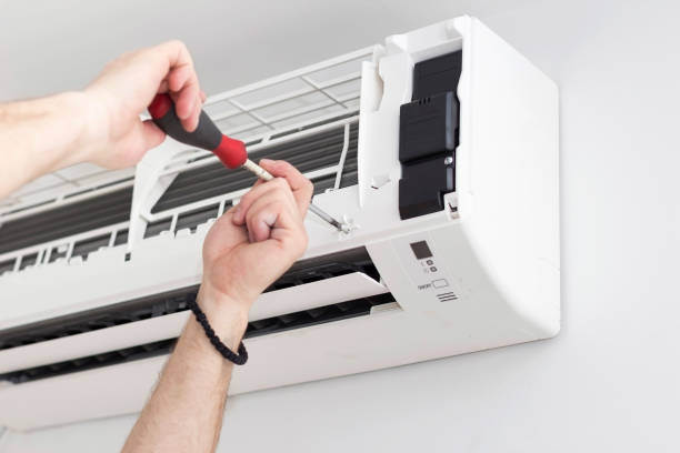 Technician repairing air conditioning unit with screwdriver