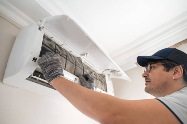 Technician in cap inspecting and cleaning wall-mounted air conditioning unit