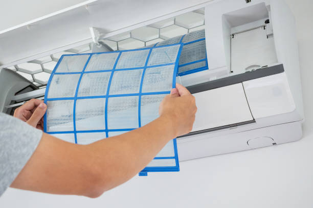 Person removing blue-lined air filter from white air conditioning unit