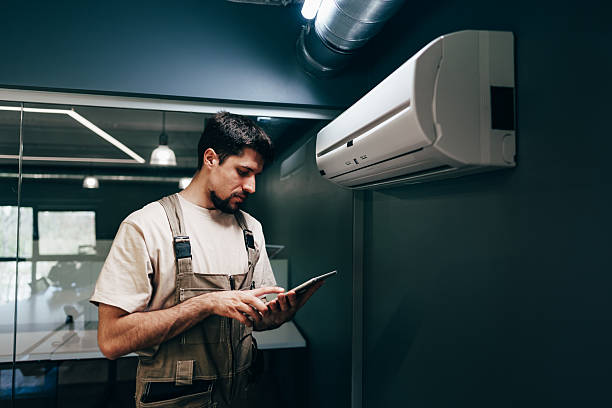 Technician checking air conditioner unit using tablet in modern office