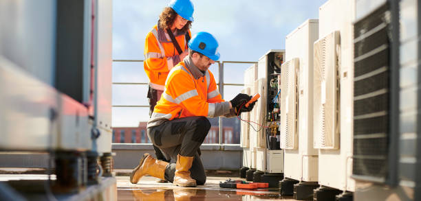 Two workers in safety gear inspect electrical equipment on rooftop