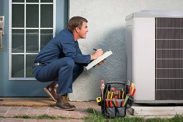 HVAC technician inspecting outdoor air conditioning unit with clipboard