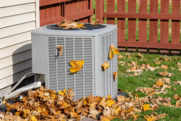 Air conditioning unit surrounded by fallen autumn leaves near wooden fence