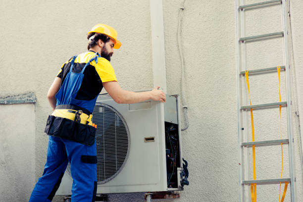 Technician in safety gear repairing an air conditioning unit near a ladder