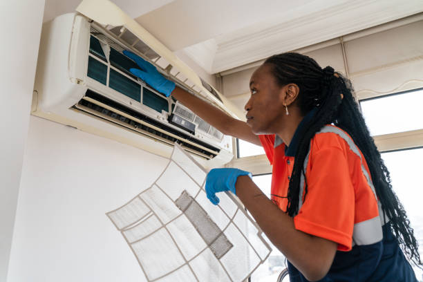 Technician in orange shirt cleaning and maintaining wall-mounted air conditioner