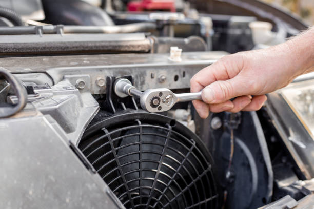 Mechanic uses ratchet wrench to repair car engine near cooling fan
