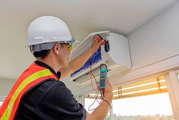 Technician in safety gear checking electrical connections on air conditioning unit