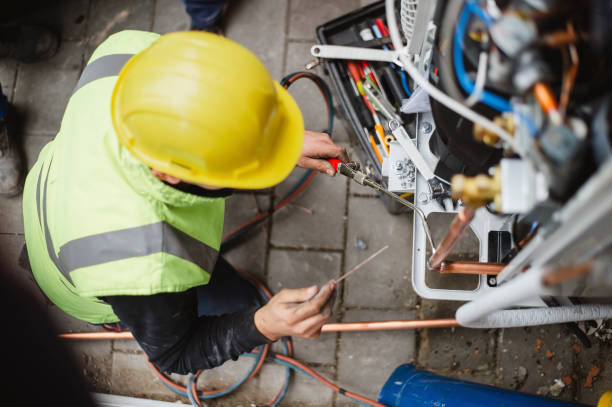 Electrician in yellow hard hat working on electrical panel with copper wires