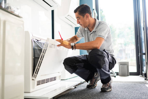 Technician crouching and checking air conditioning unit with red tool