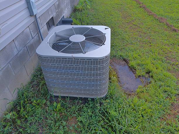 Outdoor air conditioning unit sitting on grass next to a house foundation