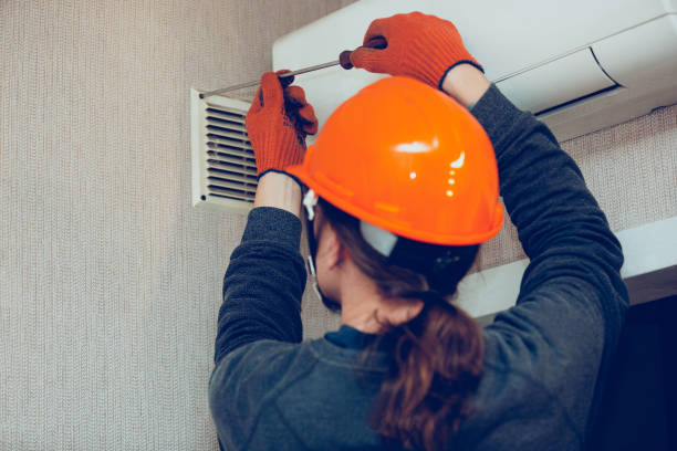 Worker in orange hard hat fixing air vent on textured wall