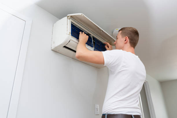 Person checking and cleaning air conditioning unit mounted on wall
