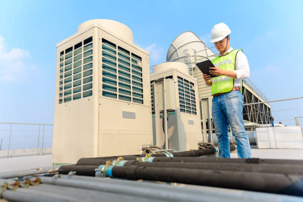 Technician in safety vest checks HVAC units on rooftop with clipboard