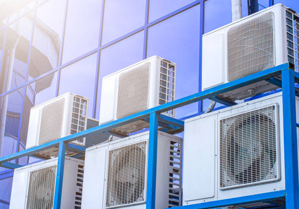 Multiple air conditioning units mounted on blue metal framework against glass building