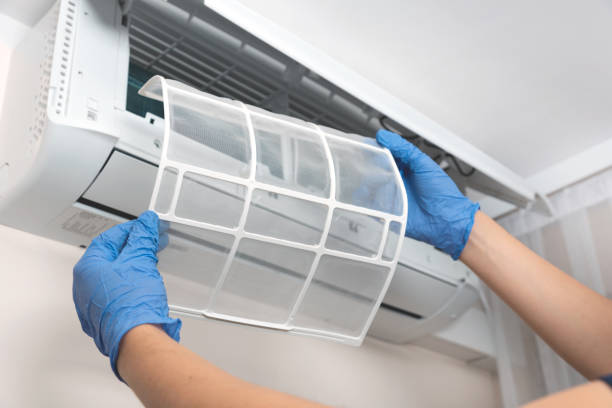 Hands in blue gloves removing air conditioner filter for cleaning