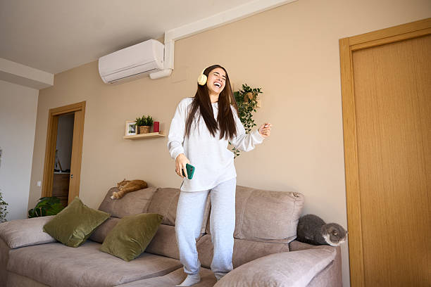 Woman in white loungewear jumping joyfully on cozy living room couch