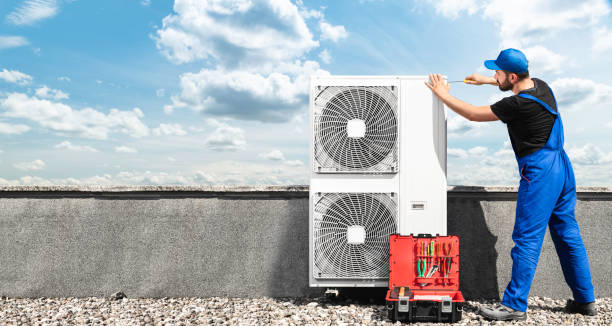 Technician in blue uniform checks outdoor air conditioning unit on roof