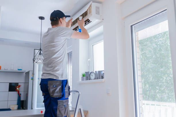Technician installing air conditioning unit on white wall near window