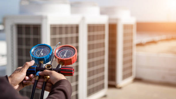 Technician using pressure gauges to check HVAC system near air conditioning units