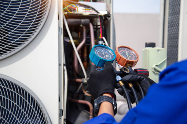 Technician checking pressure gauges on air conditioning unit's refrigerant lines