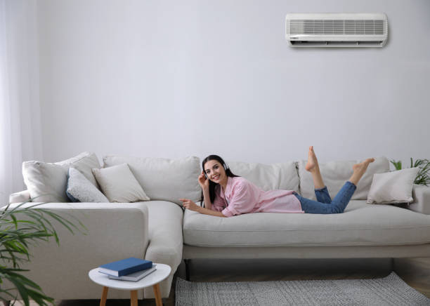 Woman relaxing on white couch, talking on phone with air conditioner above