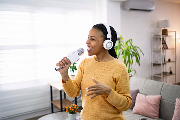 Woman in yellow sweater singing with headphones and microphone at home