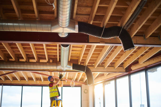 Worker in safety vest inspects HVAC ductwork on exposed wooden ceiling framework