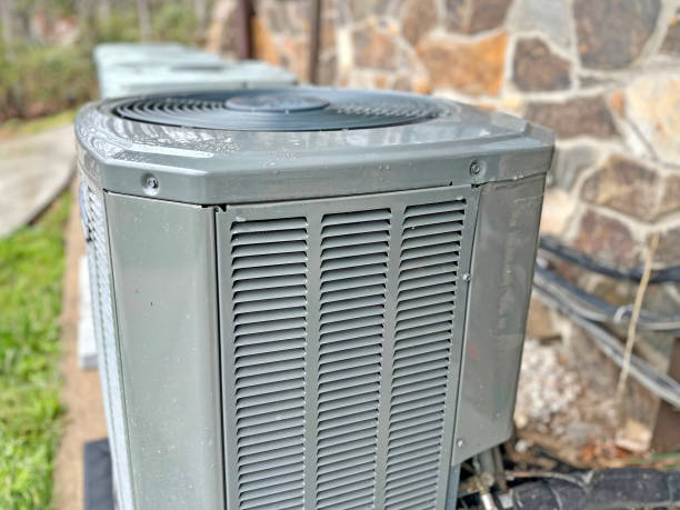 Gray outdoor air conditioning unit next to stone wall and grass