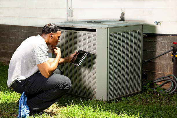 Technician inspecting air conditioning unit outside using digital tablet