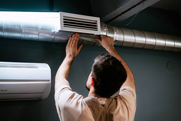 Technician adjusting air vent on industrial HVAC ductwork near wall-mounted unit